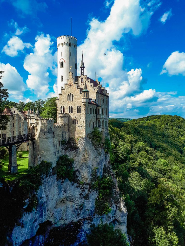 Beautiful Lichtenstein Castle perched on a cliff, surrounded by lush greenery, under a vibrant blue sky.